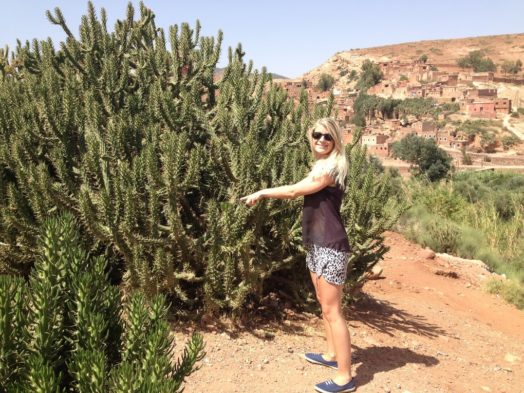 Femme près d'un cactus à Marrakech, avec village en arrière-plan. Activités à Marrakech.